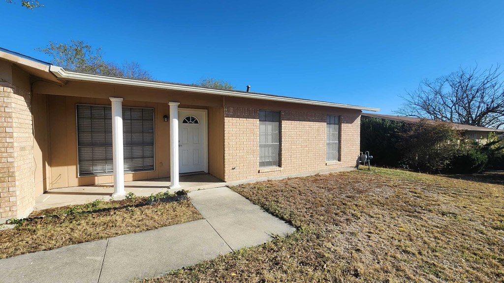 a small tan brick home with a sidewalk and a white door