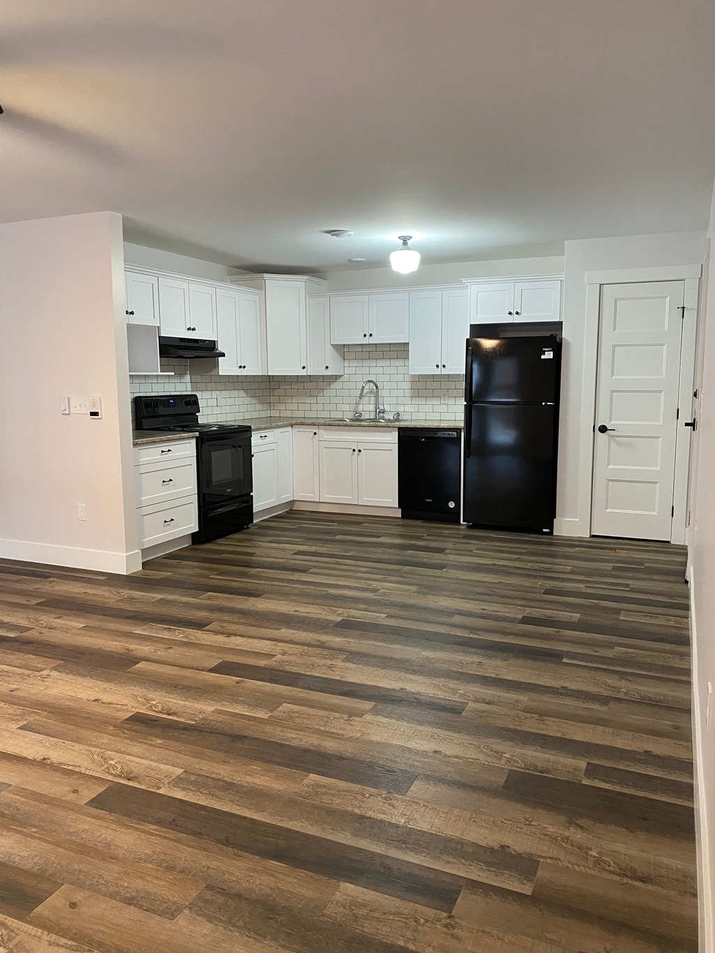 a kitchen with white cabinets and black appliances and a wooden floor