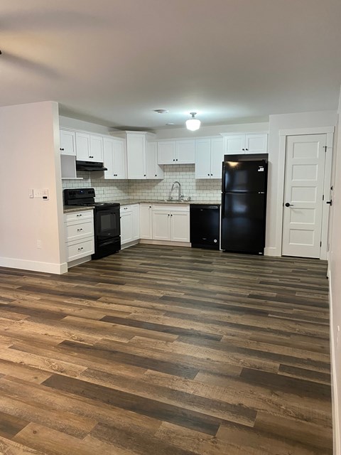 a kitchen with white cabinets and black appliances and a wooden floor