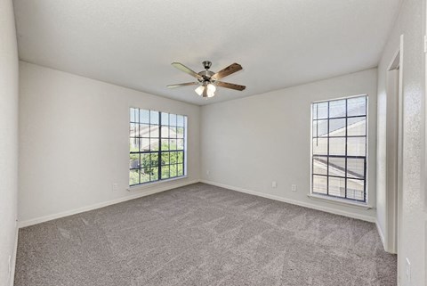 A room with a ceiling fan and two windows.