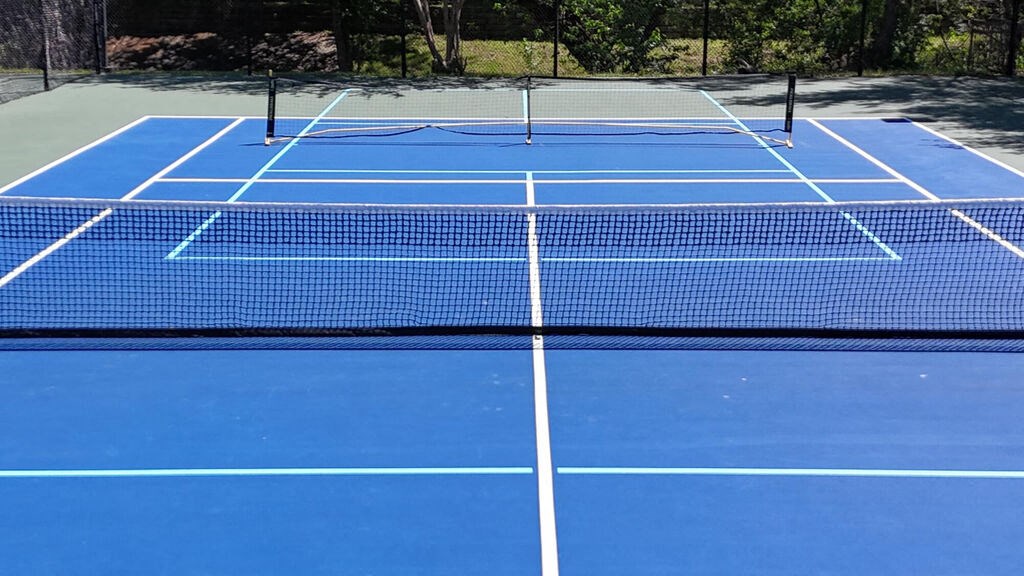 A blue tennis court with white lines and nets.