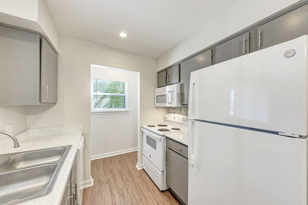 A white refrigerator is in a kitchen with white cabinets and a window.