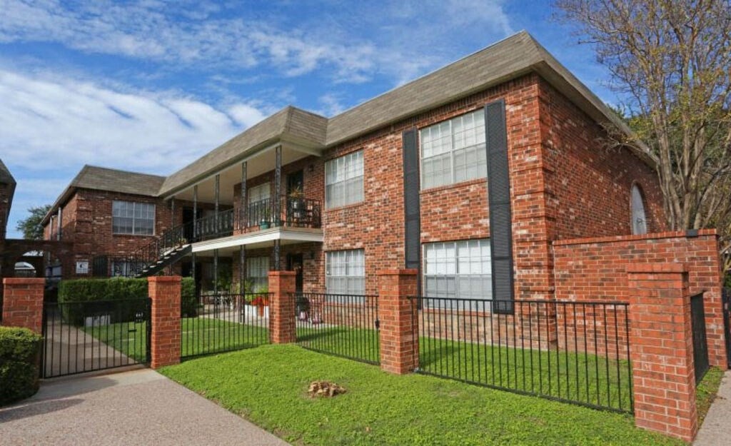 A red brick house with a black fence and a green lawn.