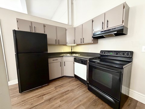 A black refrigerator and oven in a kitchen with wooden floors and white cabinets.