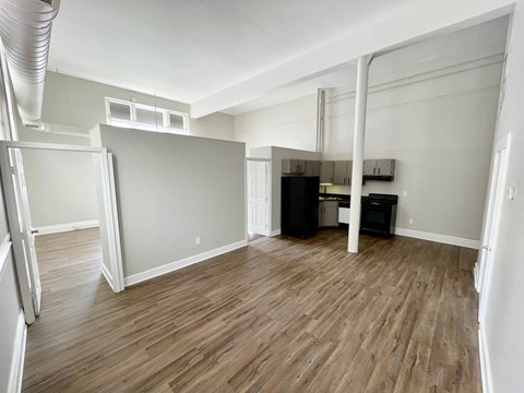 A room with wood flooring and a kitchenette in the background.