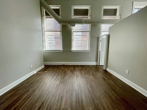 A room with wooden floors and three windows.