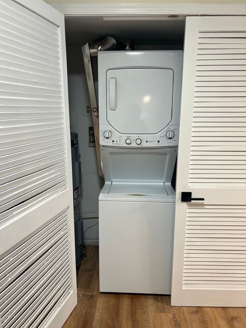 A white washing machine is in a small space between two white doors.