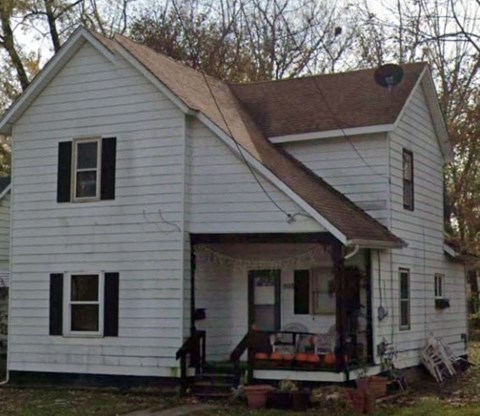 A small white house with a brown roof and a porch.