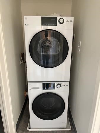 A white front load washing machine with a black door sits in a narrow laundry room.