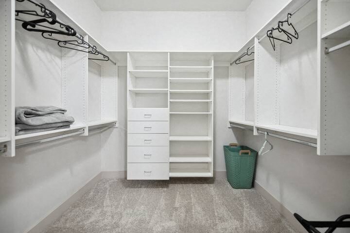 a walk in closet with white shelves and drawers