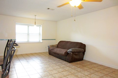 A brown couch sits in a living room with a ceiling fan and a window with blinds.