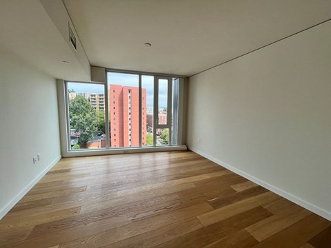 Empty room with wooden flooring and sliding glass doors.