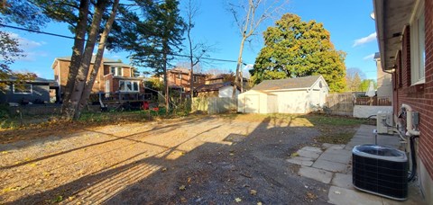 A backyard with a dirt path and a trash can.