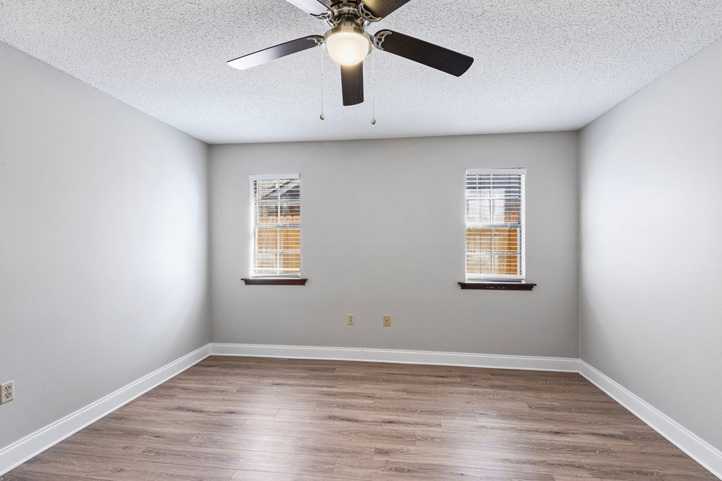 A room with a ceiling fan and two windows.