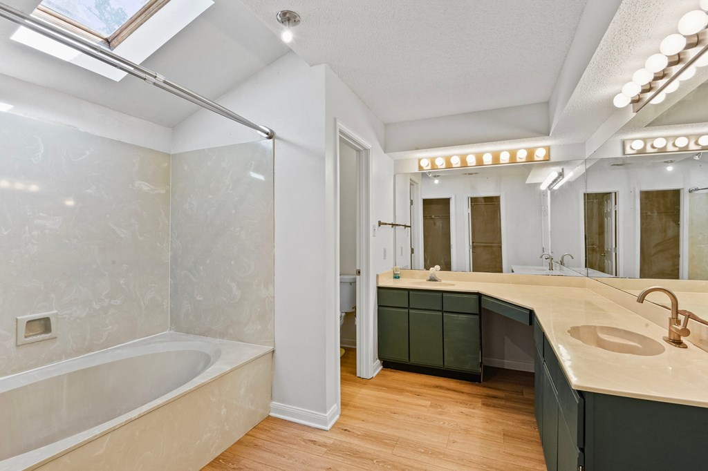 A bathroom with a skylight, a bathtub, a sink, and a vanity.