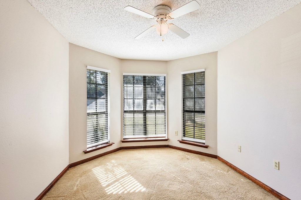 A room with a ceiling fan and two windows.