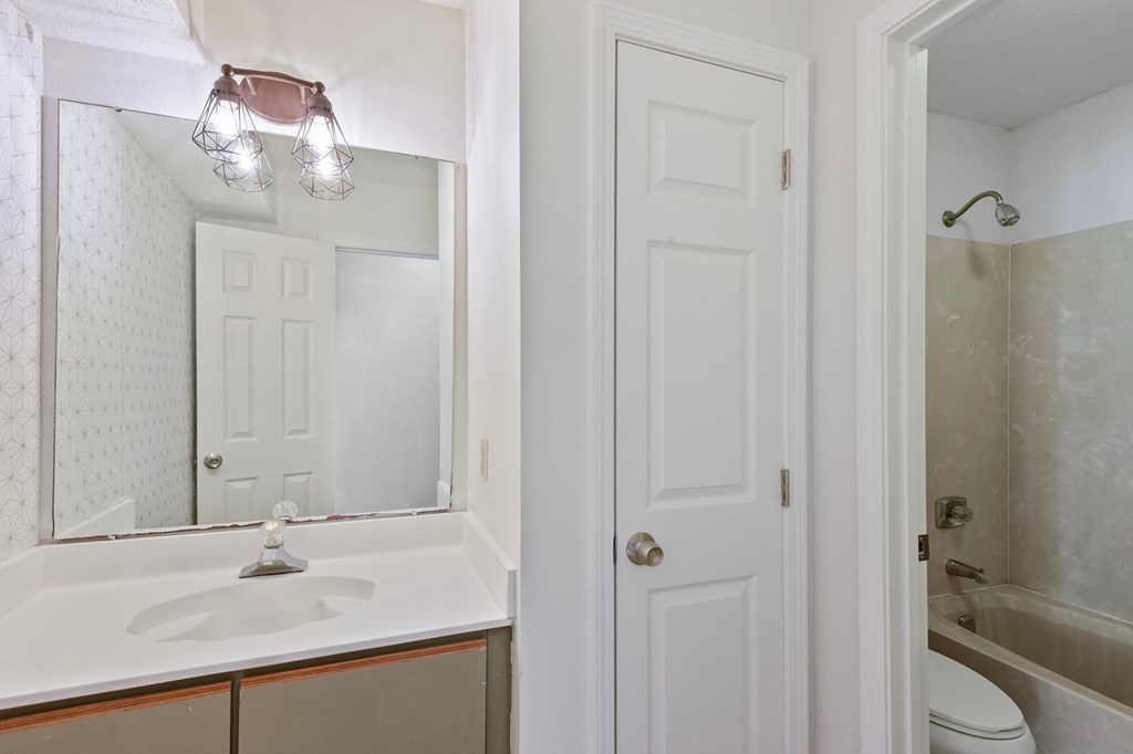 A white bathroom with a sink, mirror, toilet and shower.