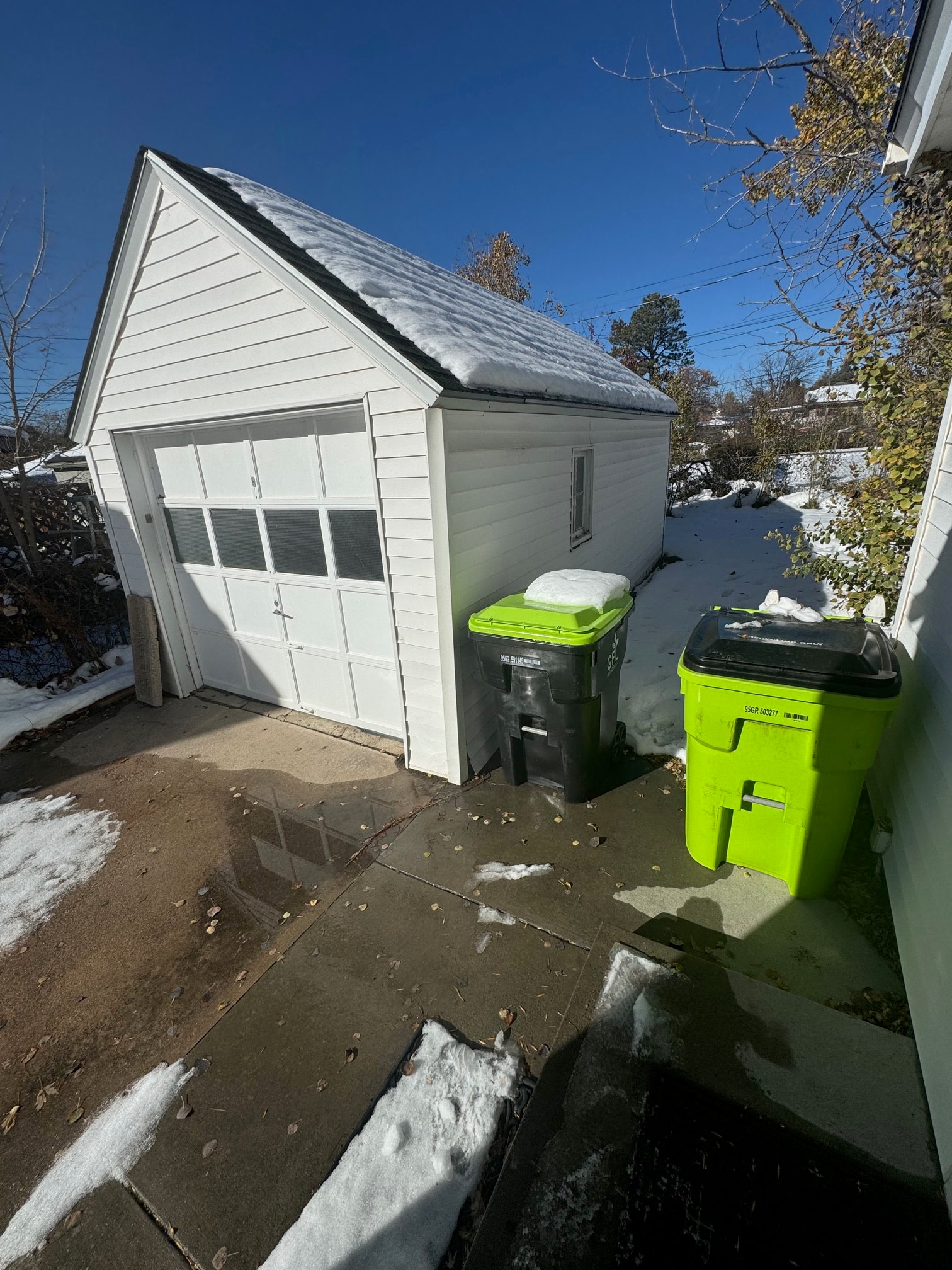the side of a garage with three trash cans on the driveway
