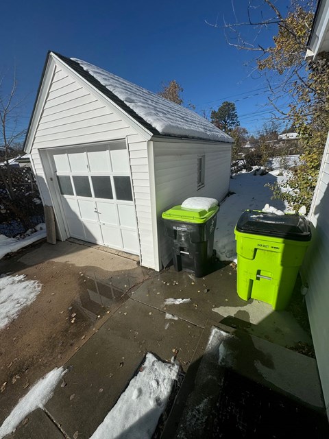 the side of a garage with three trash cans on the driveway