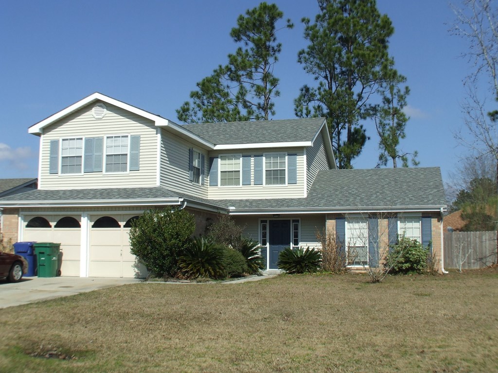 A house with a grey roof and a green trash can in front of it.
