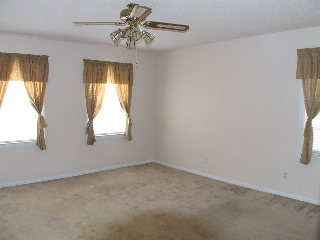 A room with a ceiling fan and two windows with curtains.