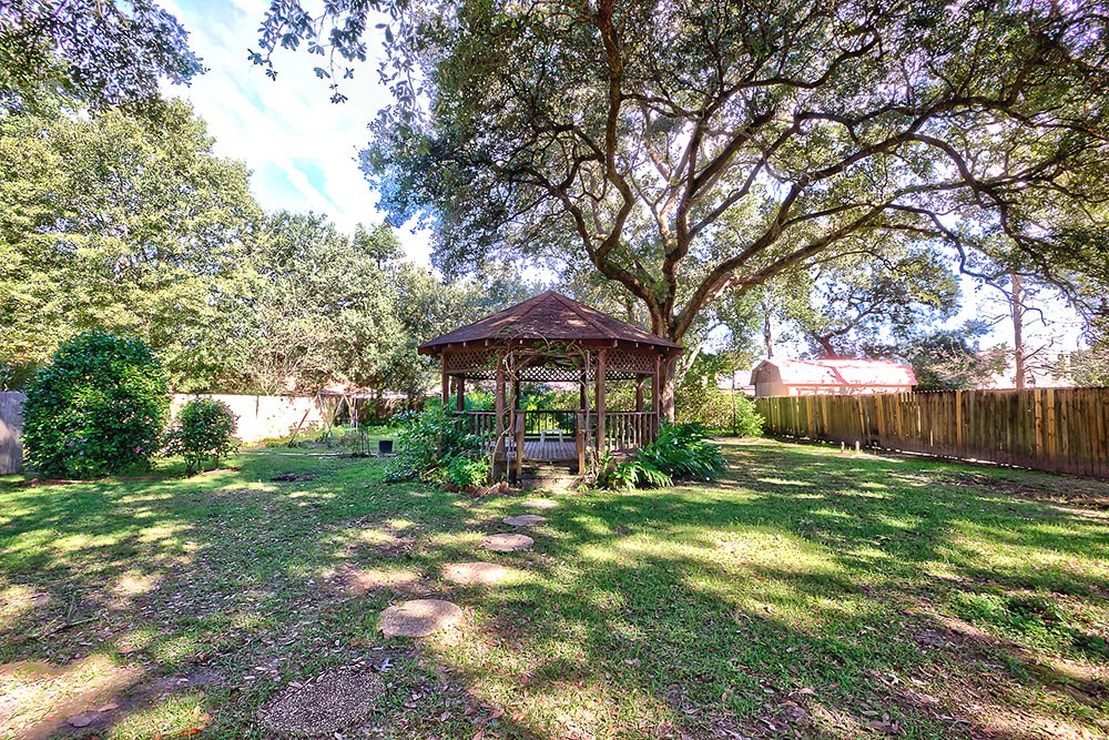 A gazebo is surrounded by trees in a sunny backyard.