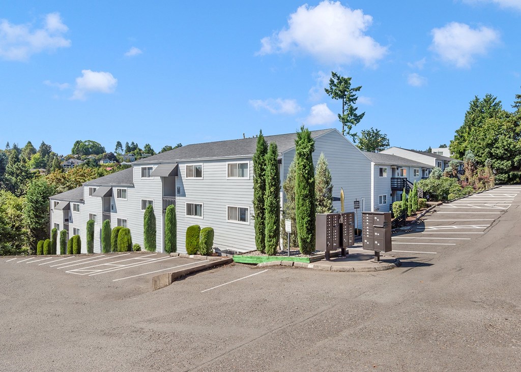 A parking lot in front of a grey building with trees.