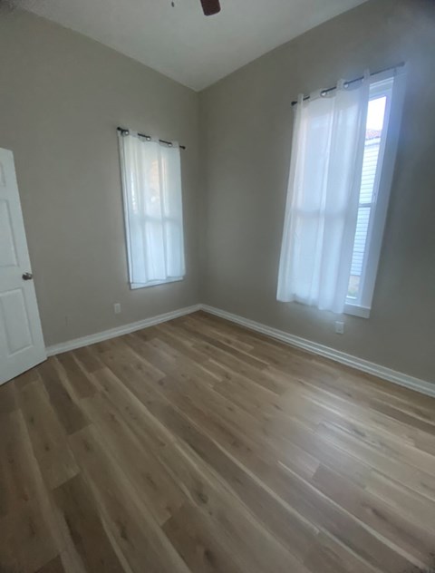 an empty room with wooden floors and two windows