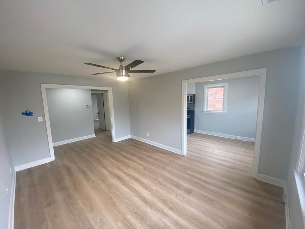 A room with a ceiling fan and light, hardwood floors, and a window with blinds.
