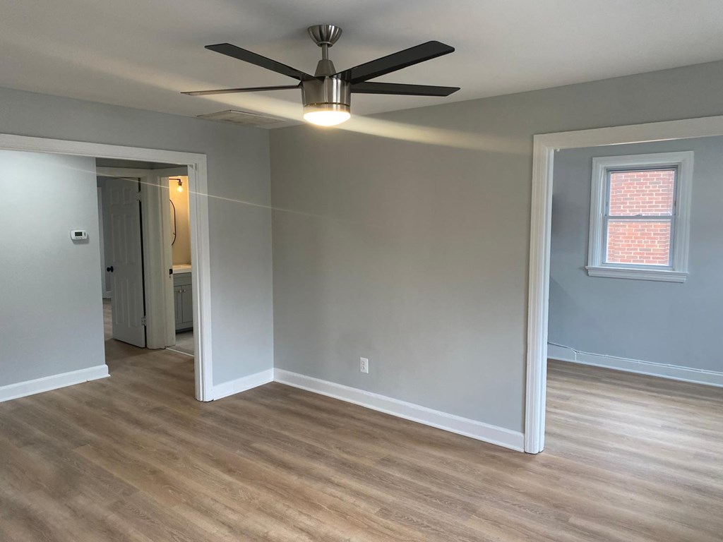 A room with a ceiling fan and light fixture, hardwood floors, and a window with a brick wall outside.