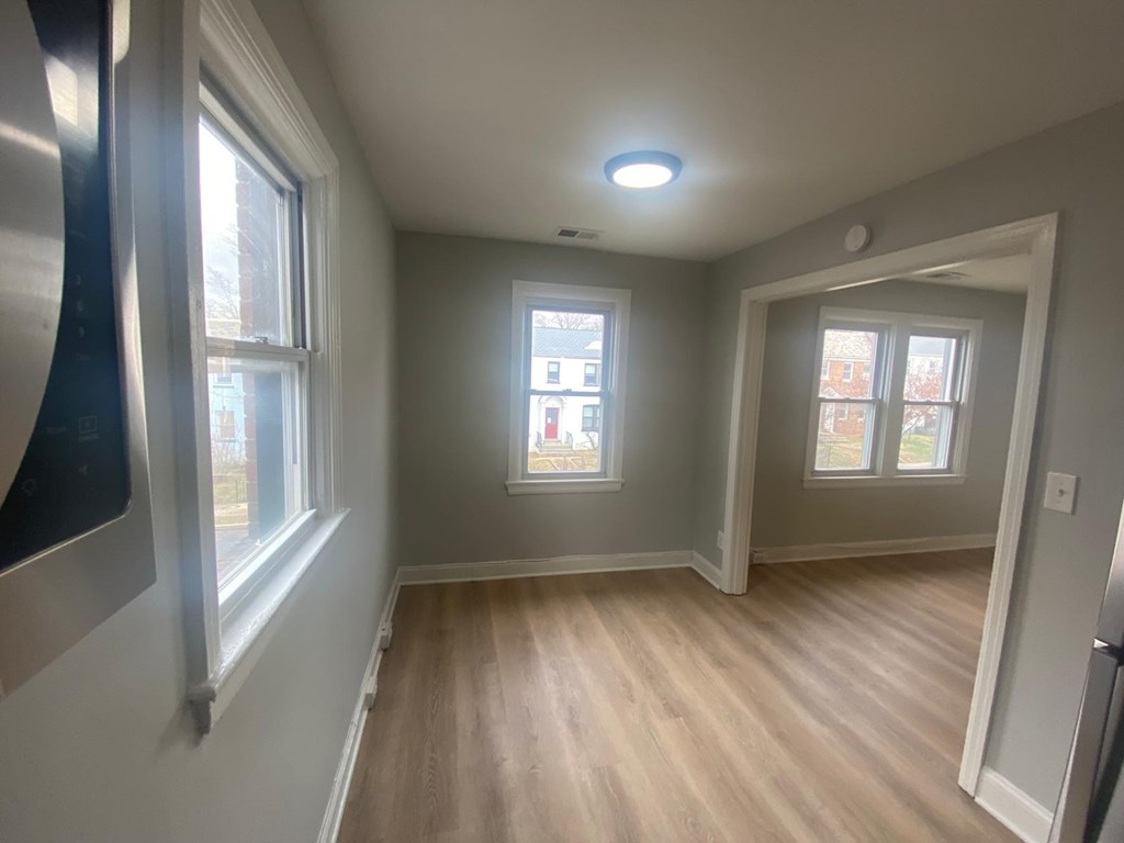 A room with light wood flooring and two windows.