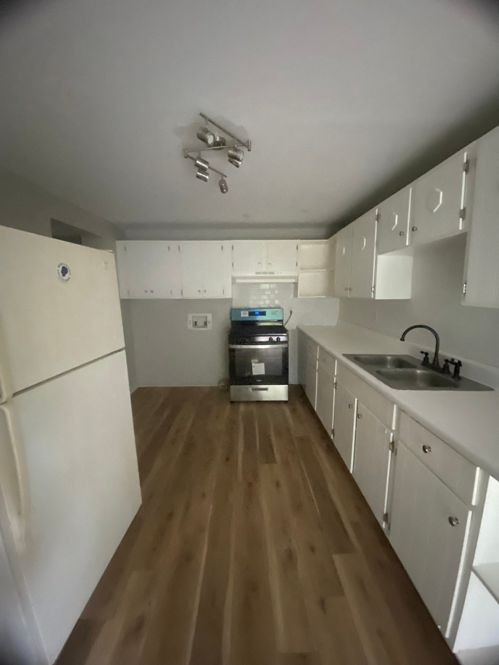 an empty kitchen with wooden floors and white cabinets