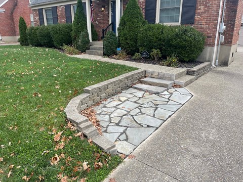 a stone retaining wall in front of a yard with grass