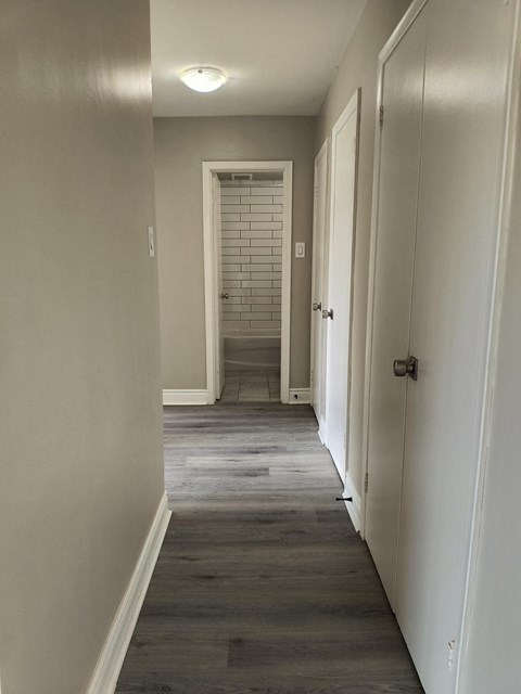 A long hallway with white walls and a brick wall in the distance.