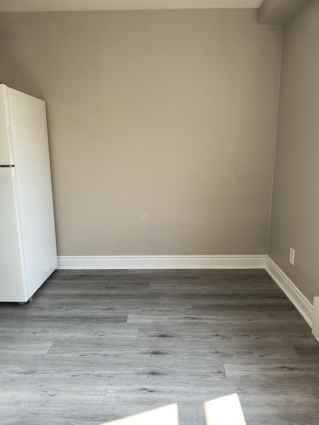 A white fridge sits in a room with wooden flooring.