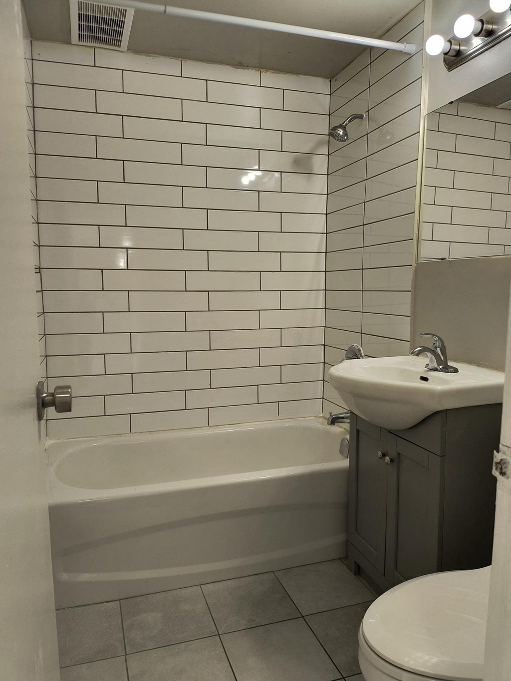 A white tiled bathroom with a bathtub, toilet, and sink.