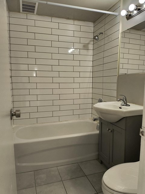 A white tiled bathroom with a bathtub, toilet, and sink.
