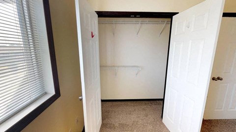 A white door is open to a room with a closet and a window with blinds.