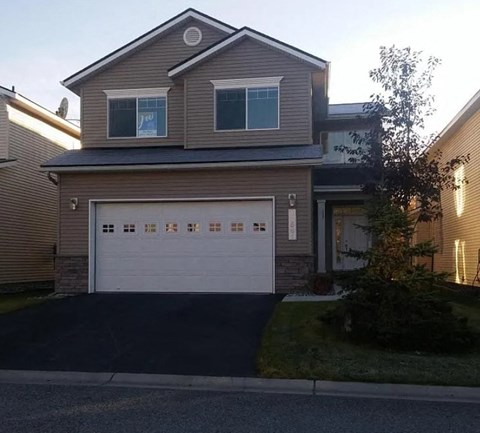 A two-story house with a garage and a tree in front.