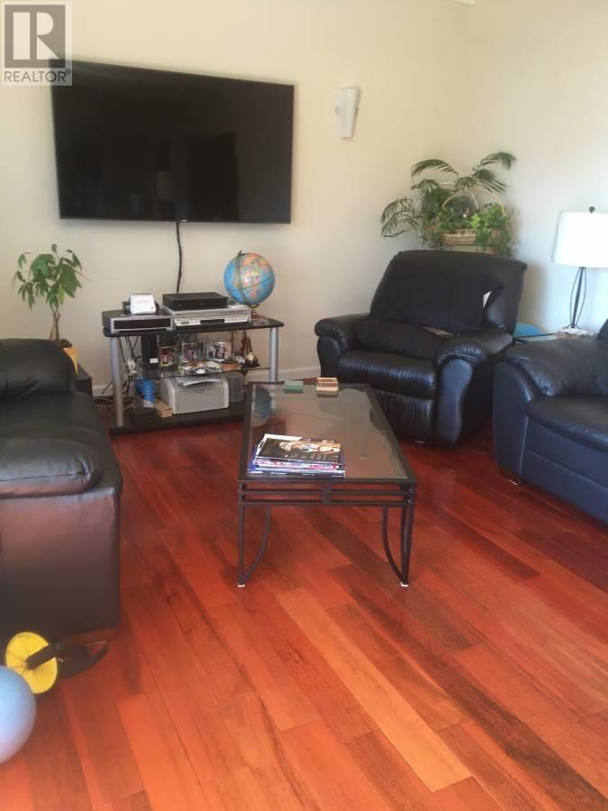 A living room with a black leather couch, a glass coffee table, and a flat screen TV mounted on the wall.