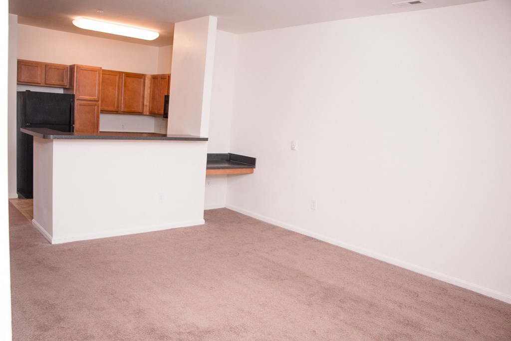 an empty room with a kitchen and a carpeted floor