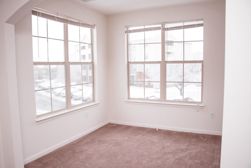 an empty room with two windows and a carpet