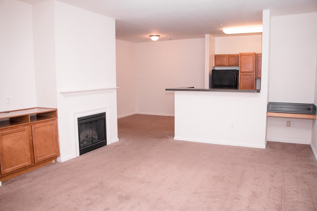 an empty living room with a fireplace and a kitchen