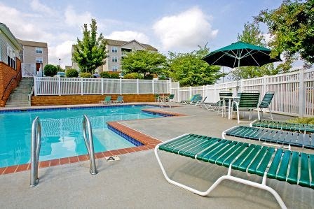 a swimming pool with green chairs and an umbrella