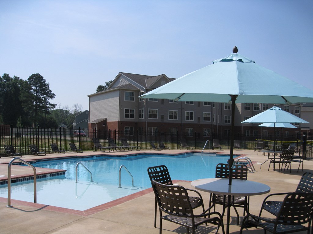 a swimming pool with tables and umbrellas in front of a building