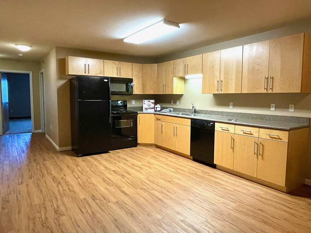 an empty kitchen with wooden floors and black appliances