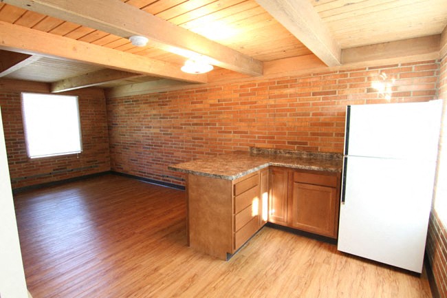 an empty kitchen with a brick wall and wood floors