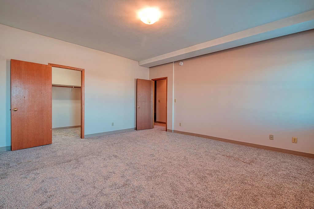 an empty living room with white carpet and a door to a closet