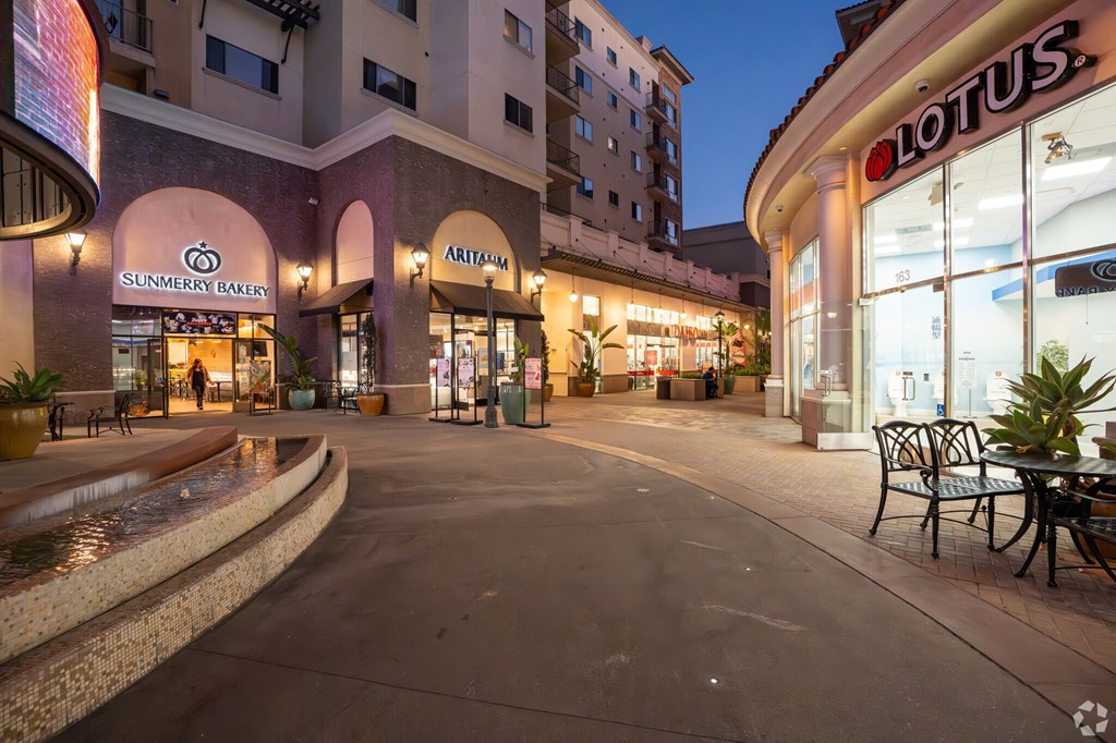 A sunken plaza with a fountain and a paved walkway with tables and chairs.