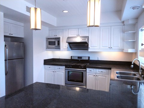A modern kitchen with a black countertop and stainless steel appliances.